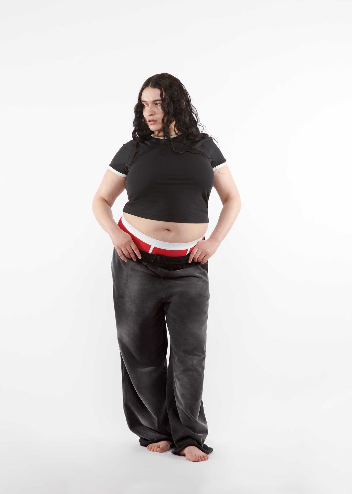 Person wearing a black crop top and gray pants on a white background